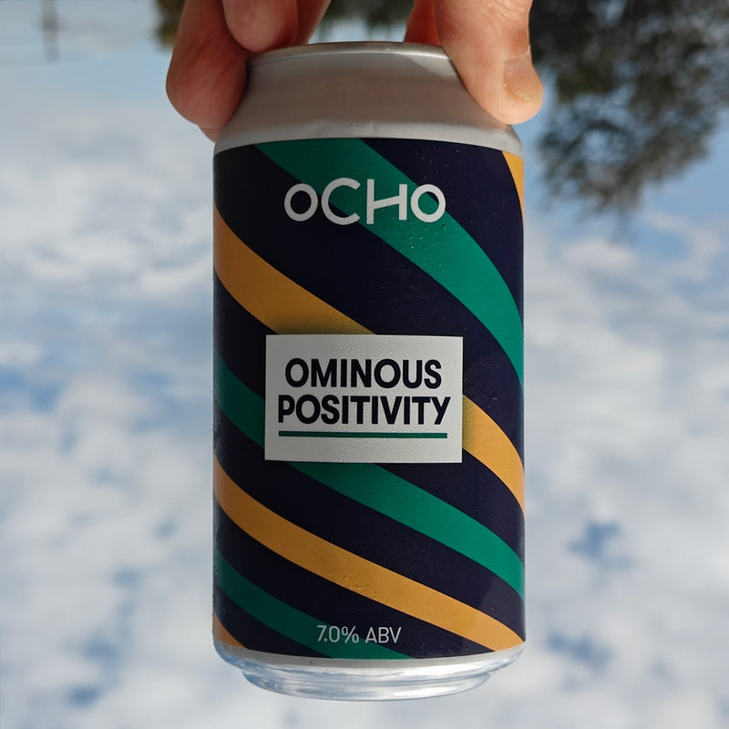 Can with 'OCHO' branding and 'Ominous Positivity' text against a blurred natural background